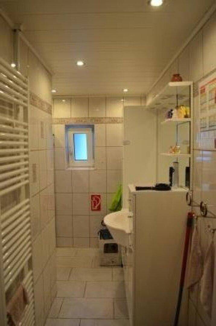 Schlichtes Badezimmer mit weißen Fliesen, Waschbecken und beheiztem Handtuchhalter.