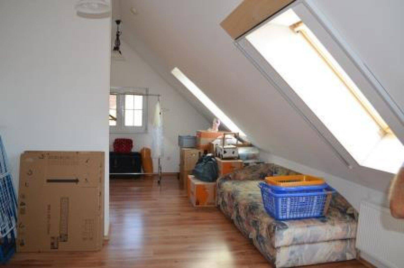 Dachzimmer mit Dachfenstern, Sofa und verschiedenen Lagergegenständen.