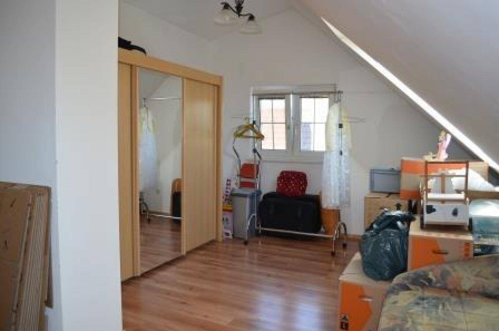 Dachzimmer mit Fenster, Spiegelschrank und Laminatboden.