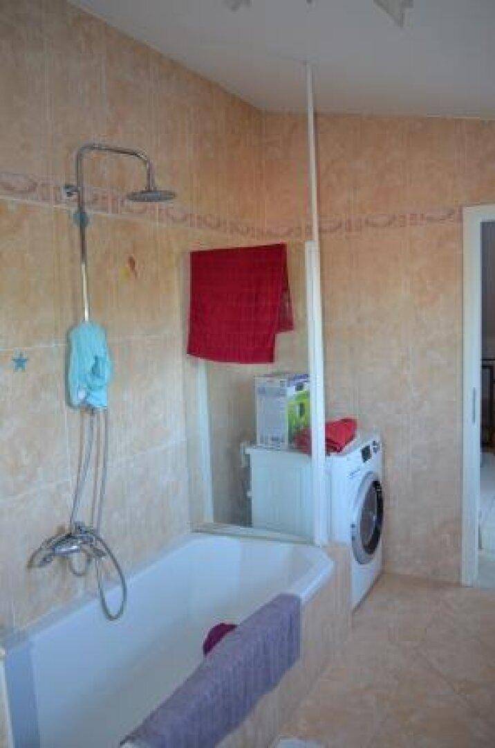 Badezimmer mit Badewanne, Duschvorrichtung und Waschmaschine, praktisch eingerichtet.