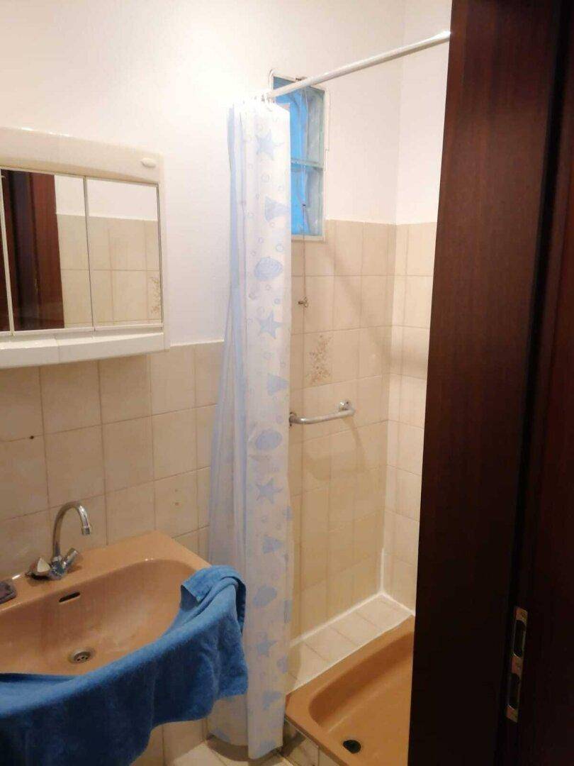 Badezimmer im Stil der 80er Jahre mit beigen Fliesen, Duschbereich und einem Waschbecken in Pastellfarbe.