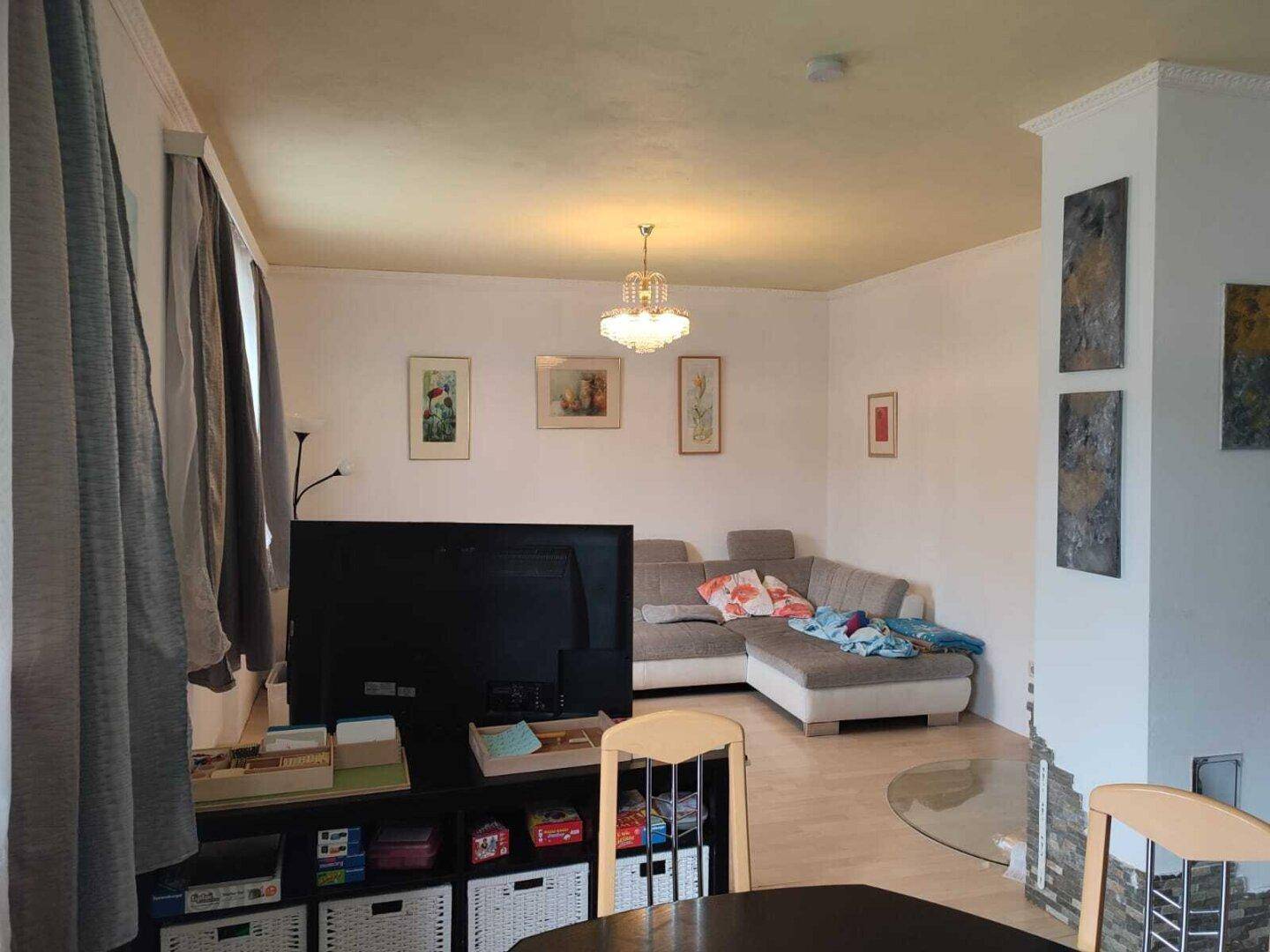 Heller Wohnbereich mit großem Ecksofa, Fernseher und dekorativen Bildern an den Wänden.
