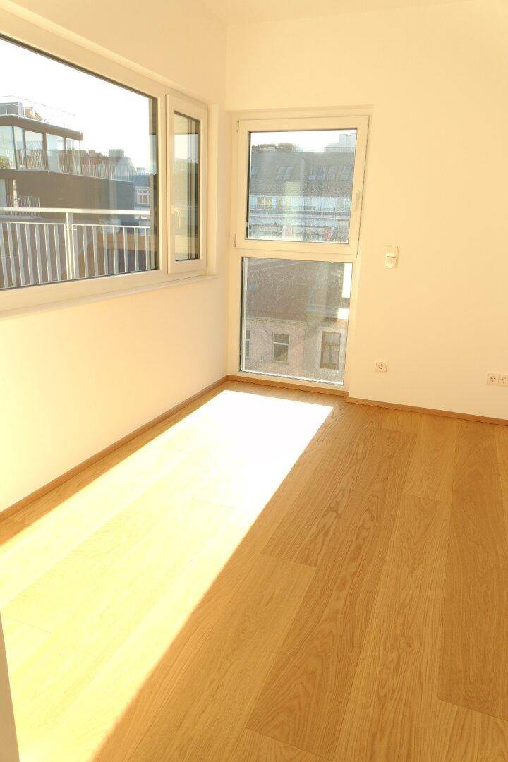 Heller Raum mit Holzboden, großen Fenstern und viel natürlichem Licht.
