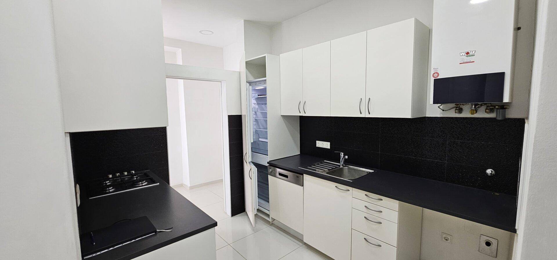 Moderne Einbauküche mit weißen Schränken, schwarzen Arbeitsplatten und integrierten Geräten.