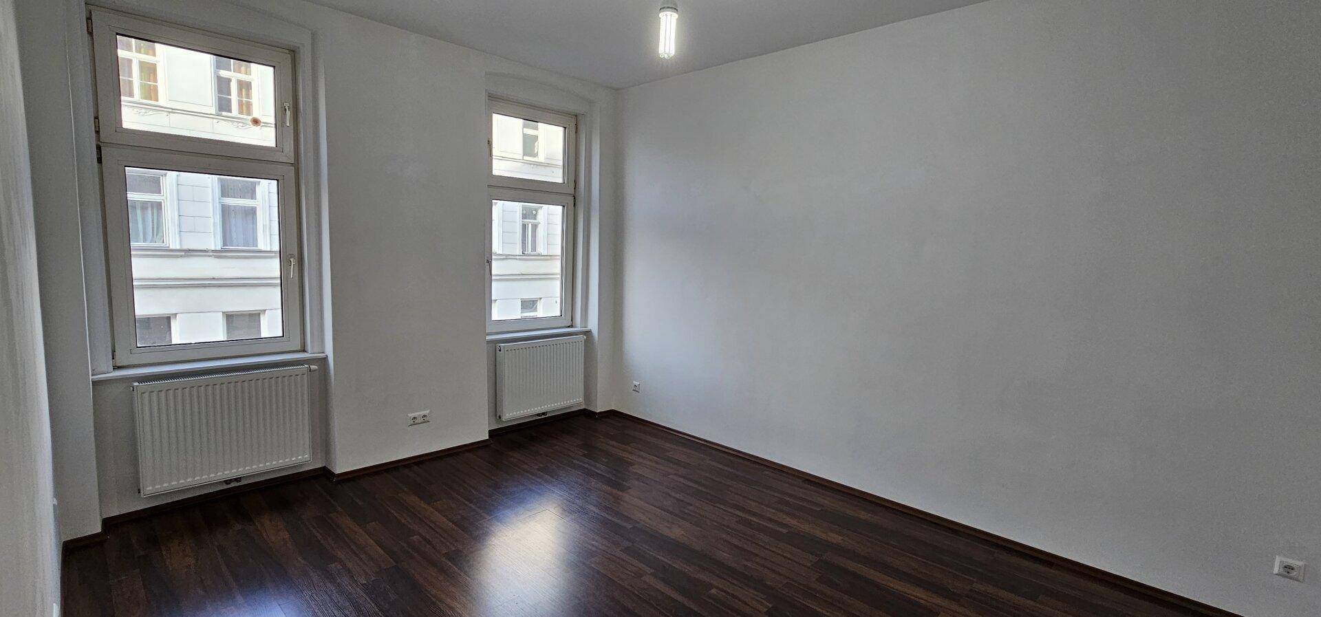 Heller, leerer Raum mit dunklem Parkettboden und Blick auf die Stadtbebauung.