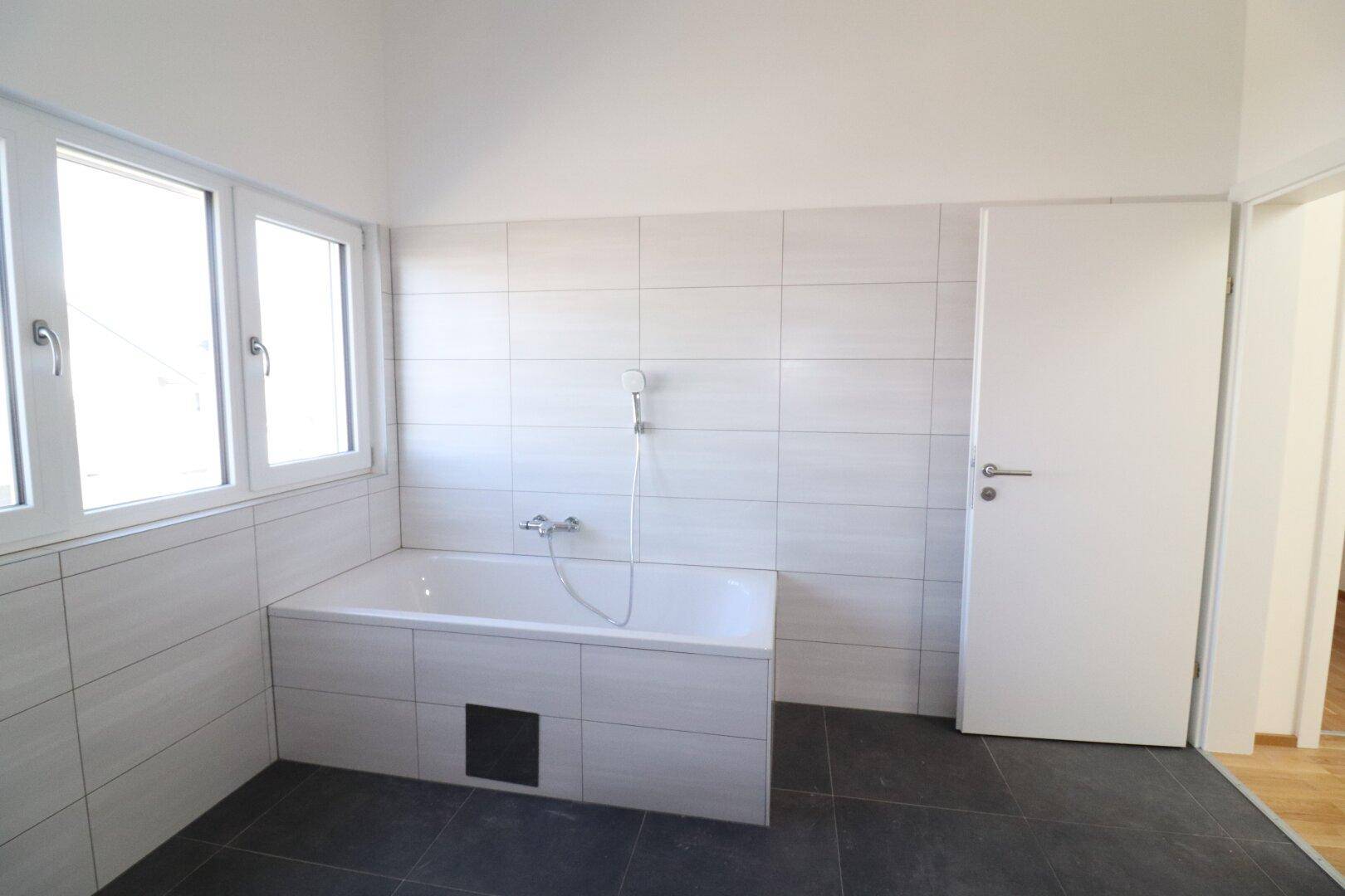Helles Badezimmer mit Badewanne, Fliesenwänden und großem Fenster.