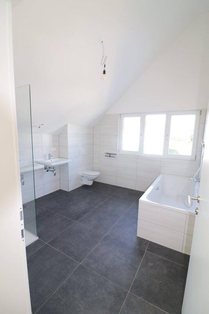 Geräumiges Badezimmer im Dachgeschoss mit Badewanne, Dusche und Fliesenboden.