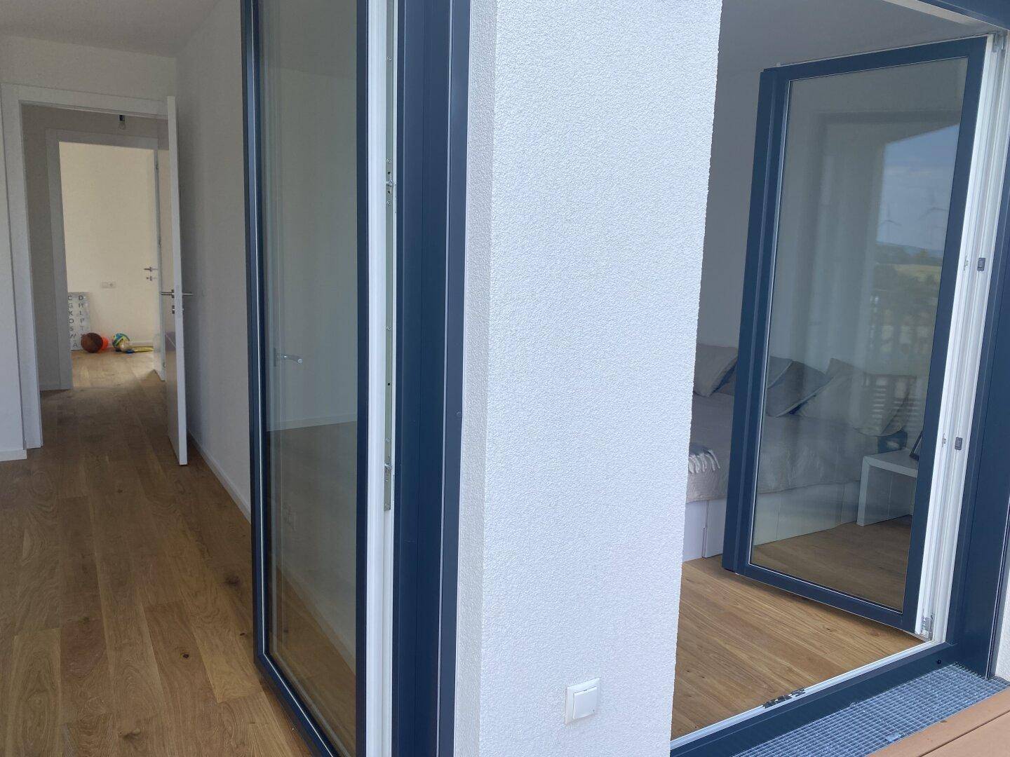 Heller Innenbereich mit Holzboden und großem Glasfenster, das Zugang zu einem Balkon bietet.