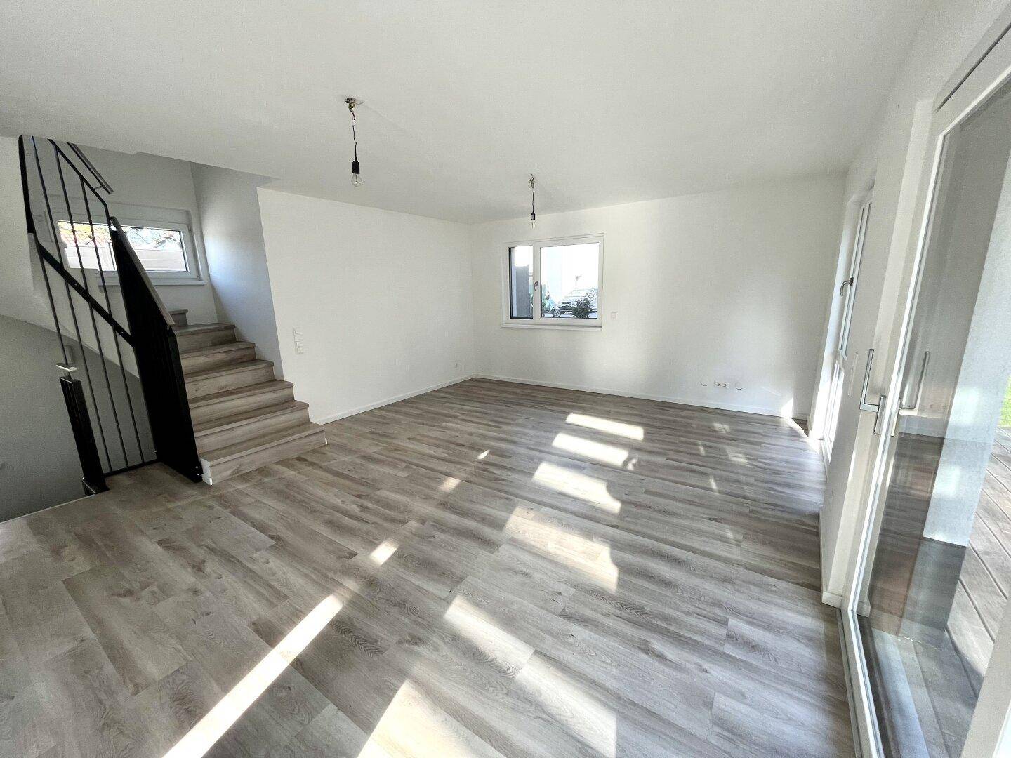 Helles Wohnzimmer mit Treppenaufgang und Laminatboden, bereit zur individuellen Gestaltung.