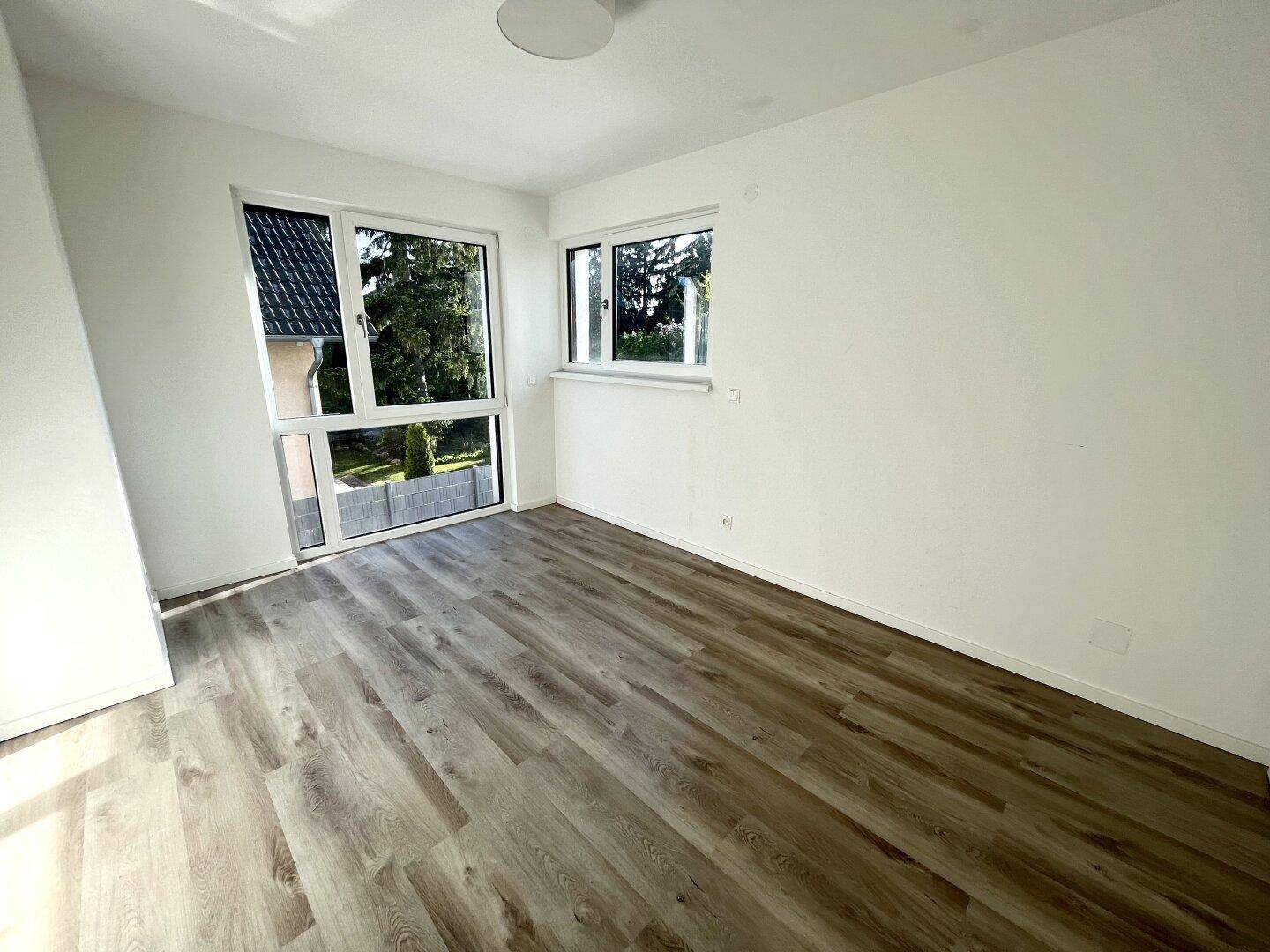 Helles Schlafzimmer mit Laminatboden und großen Fenstern, die viel Tageslicht hereinlassen.