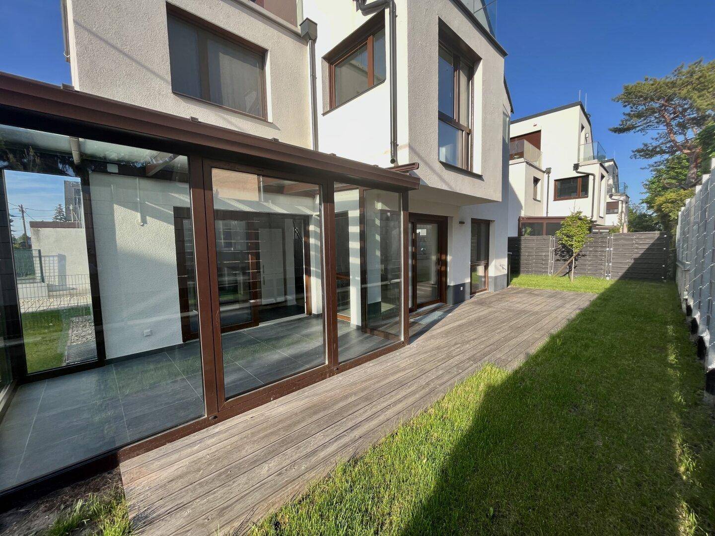Seitlicher Gartenbereich mit Holzterrasse und Zugang zum Wintergarten des Hauses.