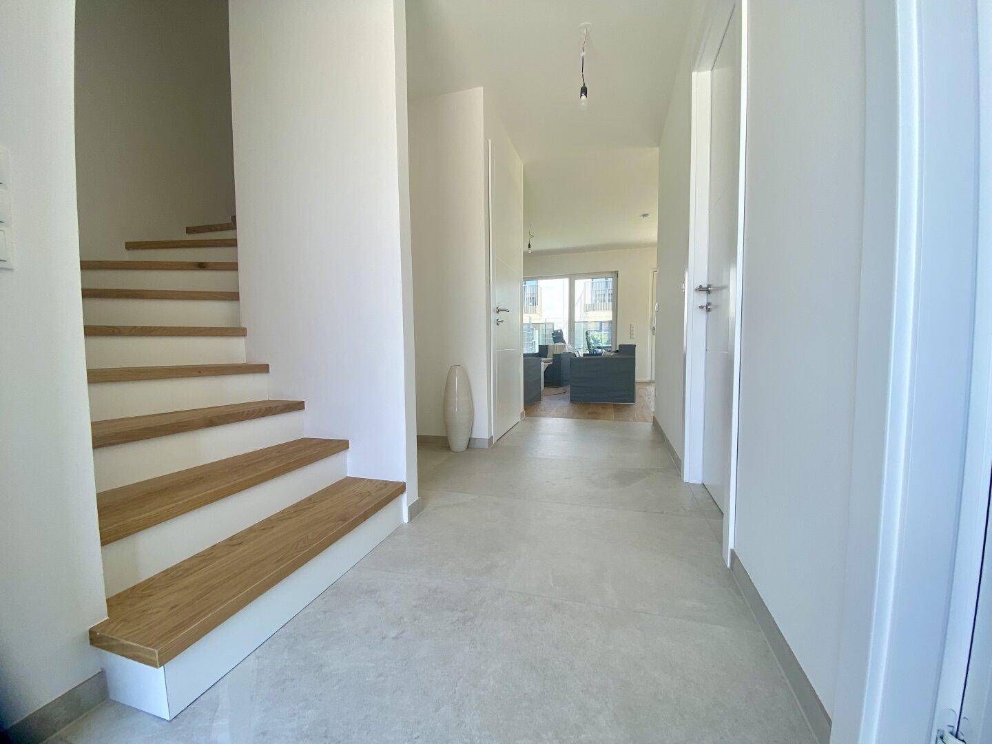 Heller Flur mit Holztreppe und Fliesenboden, der zu den Wohnbereichen führt.