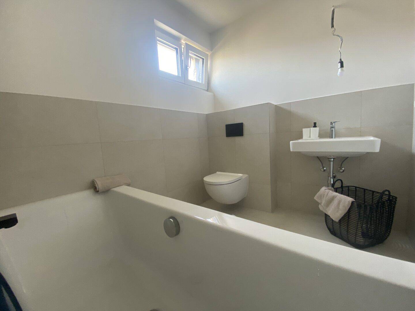 Modernes Badezimmer mit Badewanne, Wand-WC, Waschbecken und Fenster.