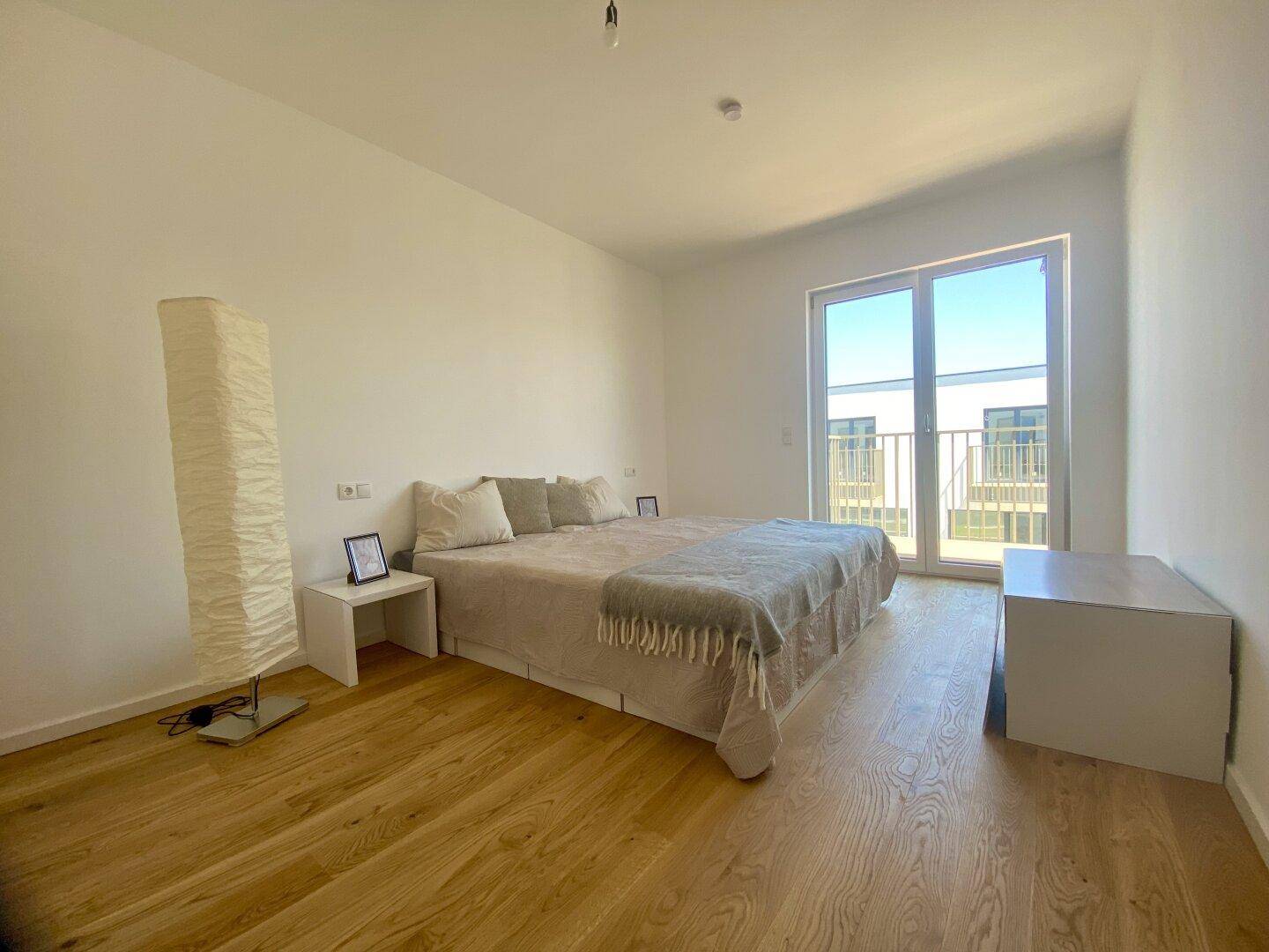 Helles Schlafzimmer mit großem Bett, Holzboden und direktem Zugang zu einem Balkon.