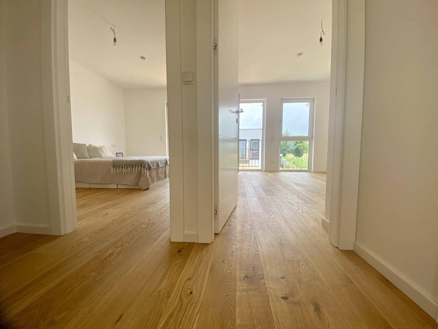Heller Flur mit Holzboden, der zu mehreren Zimmern führt, darunter ein Schlafzimmer.