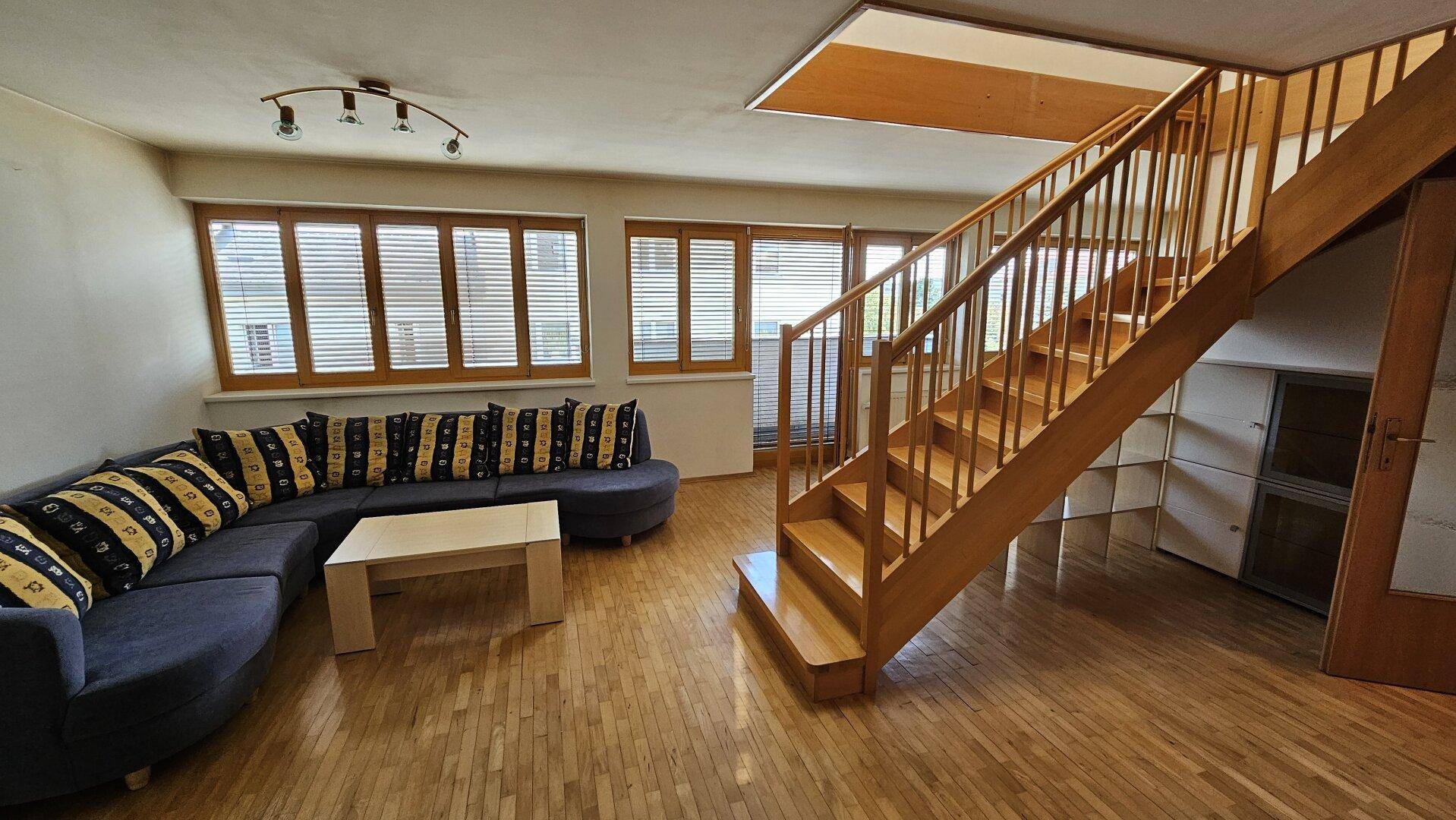 Geräumiges Wohnzimmer mit Holztreppe, Parkettboden und bequemer Sitzecke.