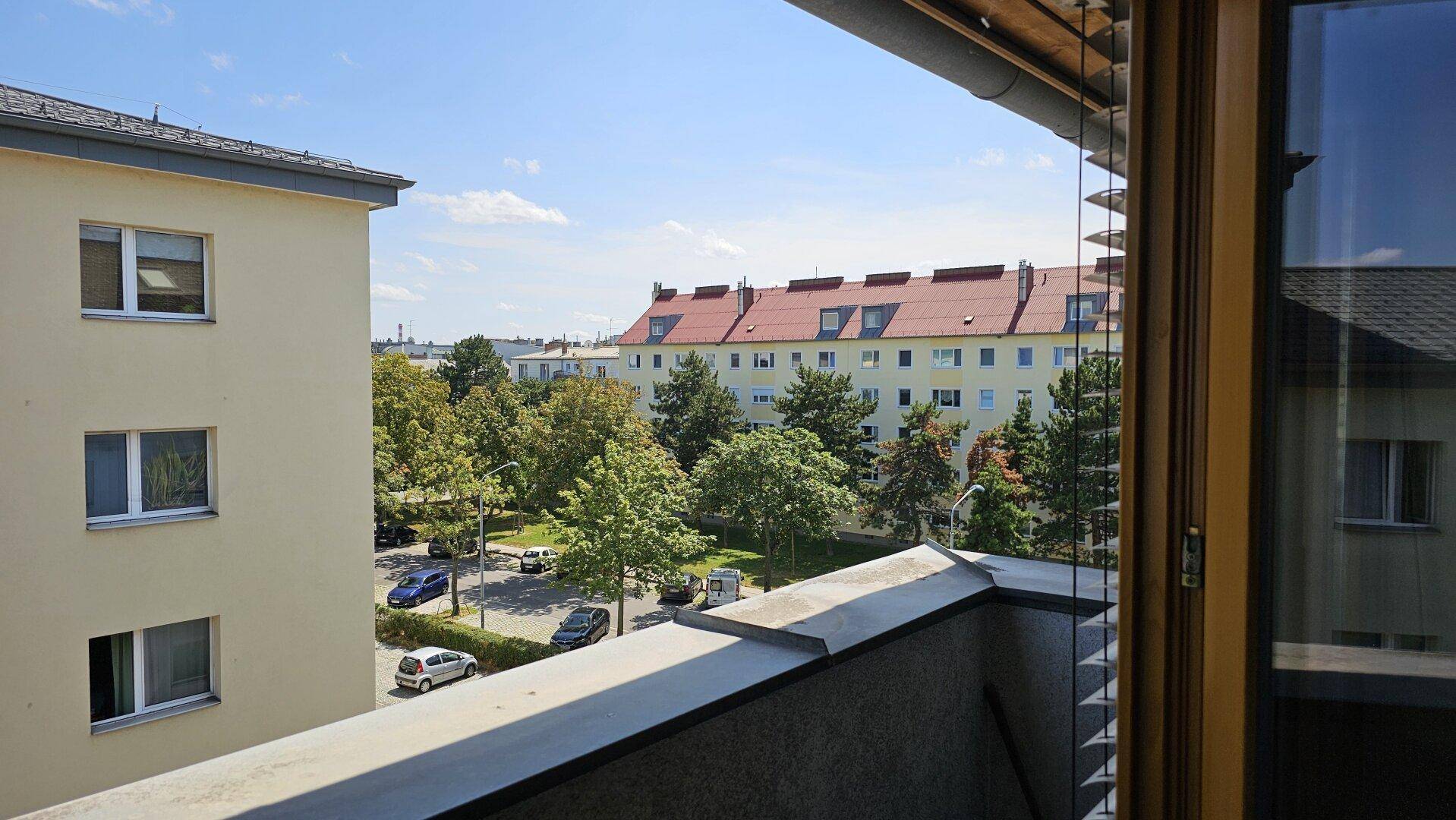 Blick vom Balkon auf die umliegenden Gebäude, Bäume und den Innenhof.