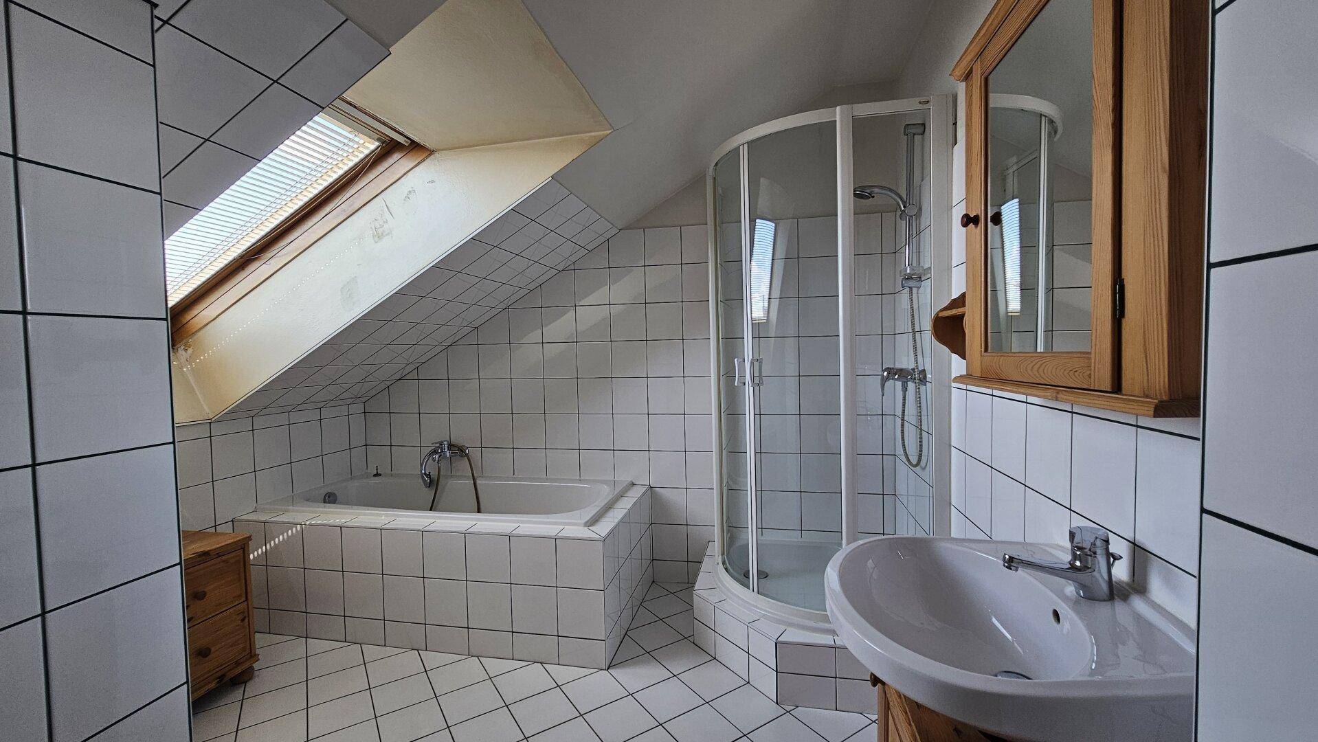 Badezimmer im Dachgeschoss mit Badewanne, Duschkabine und Dachfenster.