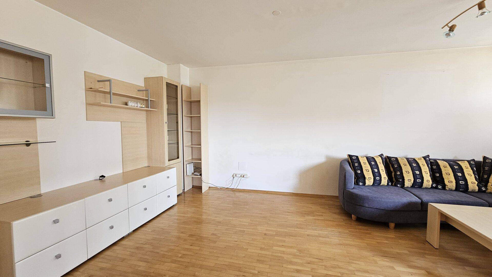 Helles Wohnzimmer mit Parkettboden, moderner Wohnwand und gemütlicher Couch.