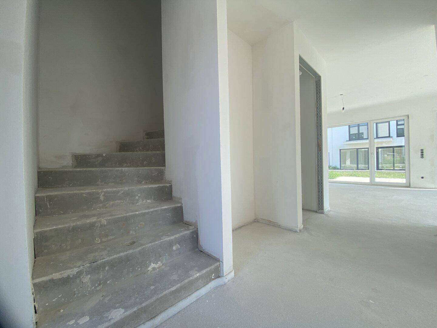 Unfertiger Flur mit Betontreppe und -boden, der den Zugang zu weiteren Räumen ermöglicht.