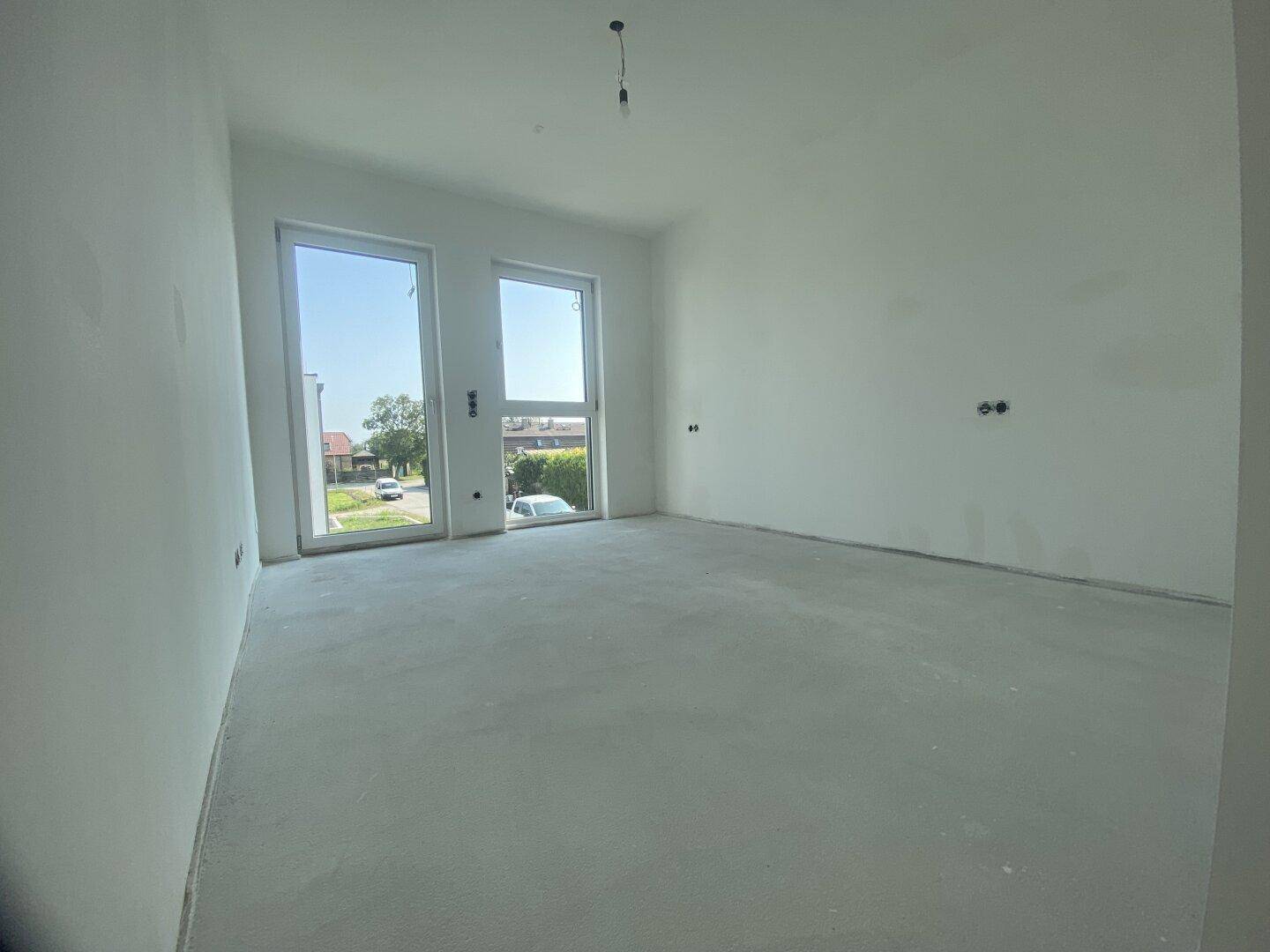 Unfertiges Zimmer mit großen Fenstern und Betonboden, ideal für Schlafzimmer oder Büro.
