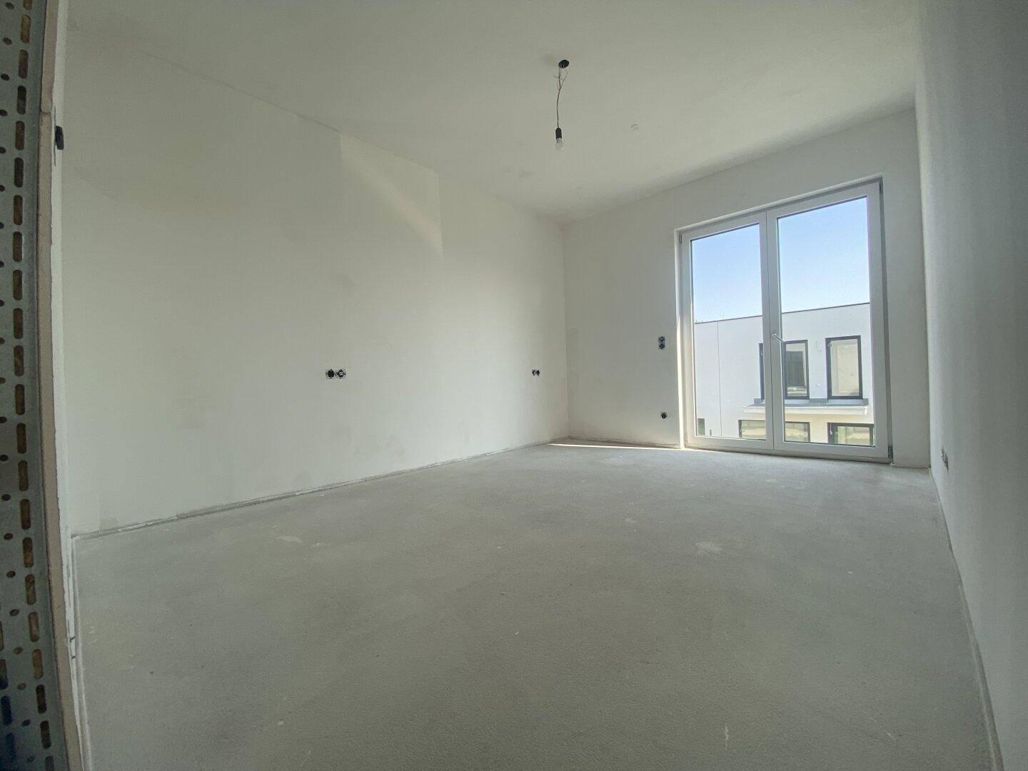 Heller, unfertiger Raum mit Betonboden und großer Glasfront, wartet auf Fertigstellung.