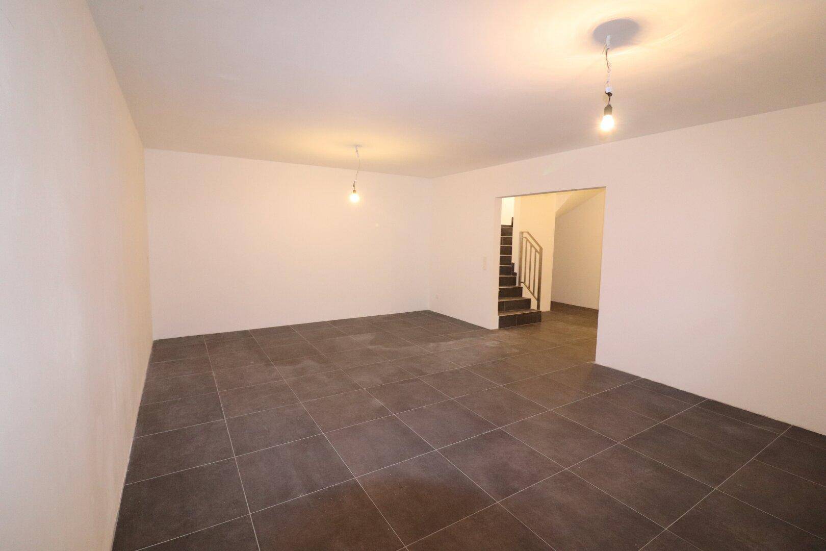 Geräumiger Kellerraum mit dunklem Fliesenboden und Zugang zu einer Treppe.