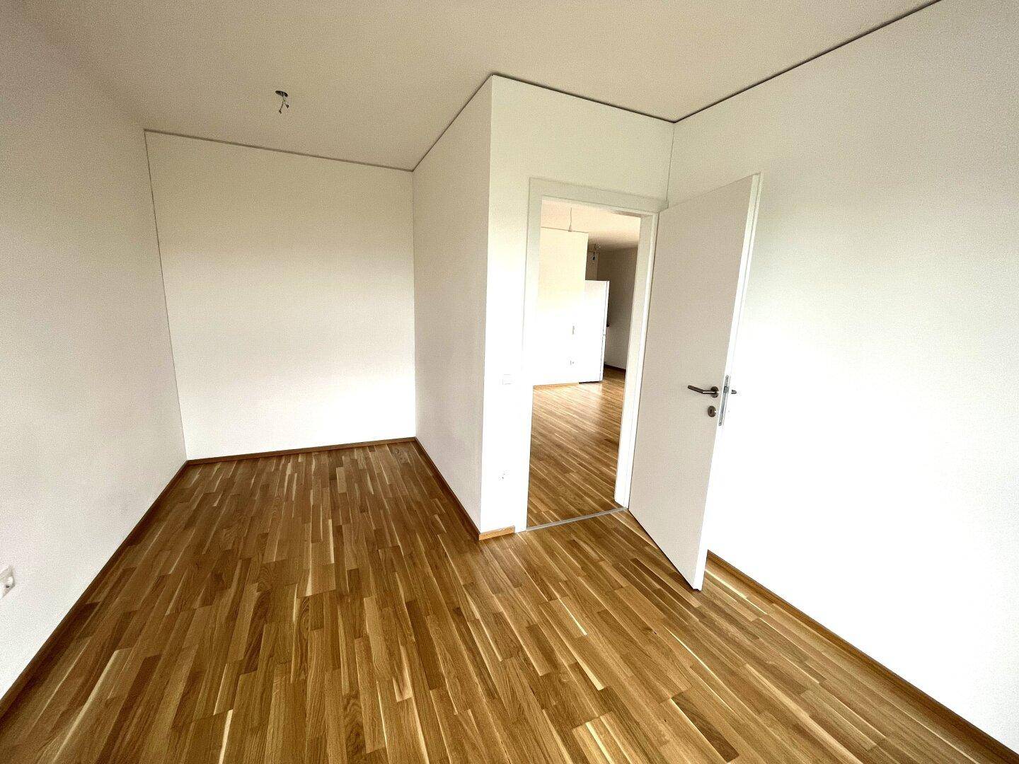 Leeres Kinderzimmer mit Parkettboden und viel Tageslicht, bereit zur Gestaltung.