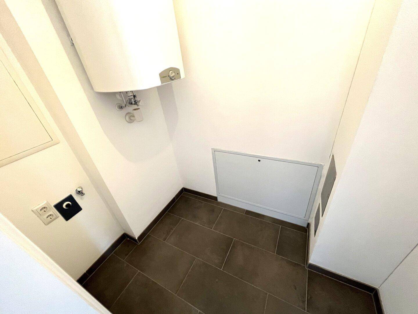 Praktischer Abstellraum mit Warmwasserboiler und Fliesenboden für Haushaltsgeräte.