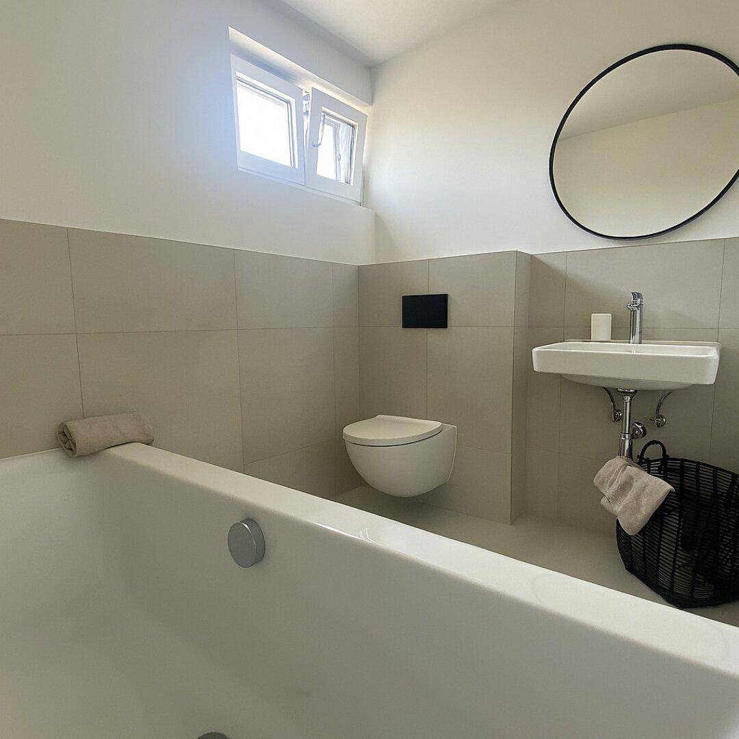Modernes Badezimmer mit Badewanne, Wand-WC und Fenster für Tageslicht.