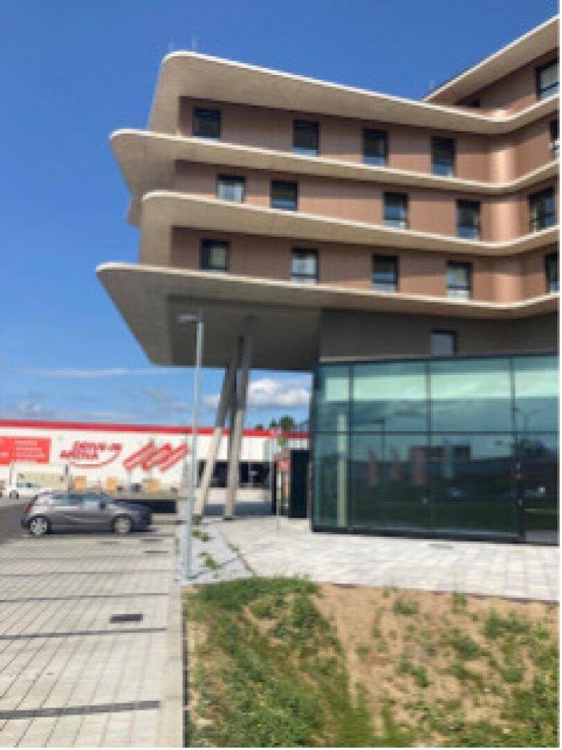 Moderne Architektur des Gebäudes mit geschwungenen Balkonen und einer weitläufigen Glasfassade im Erdgeschoss.
