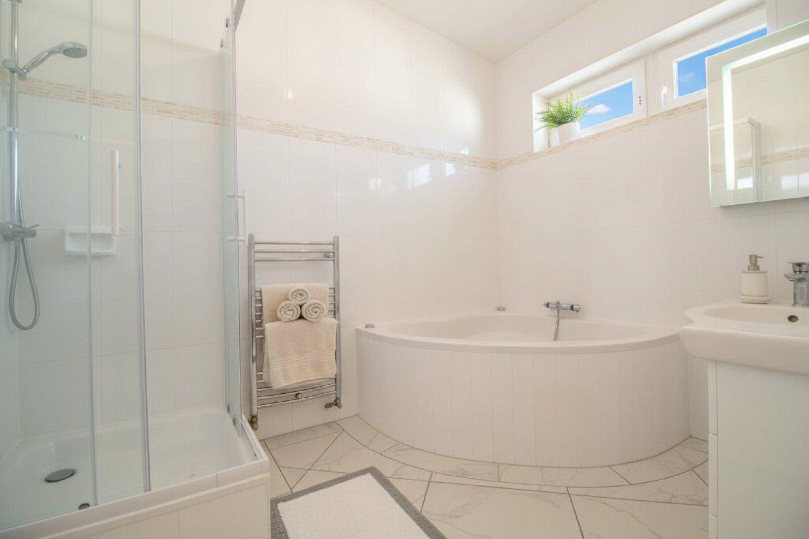 Helles Badezimmer mit Eckbadewanne, separater Dusche, weißen Fliesen und beheiztem Handtuchhalter.