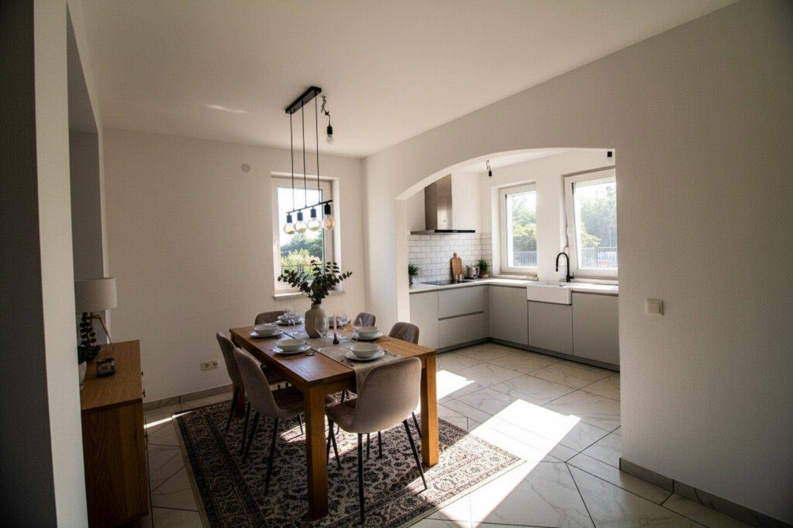 Heller Essbereich mit Holztisch und Stühlen, angrenzend an eine moderne Küche durch einen Bogen.