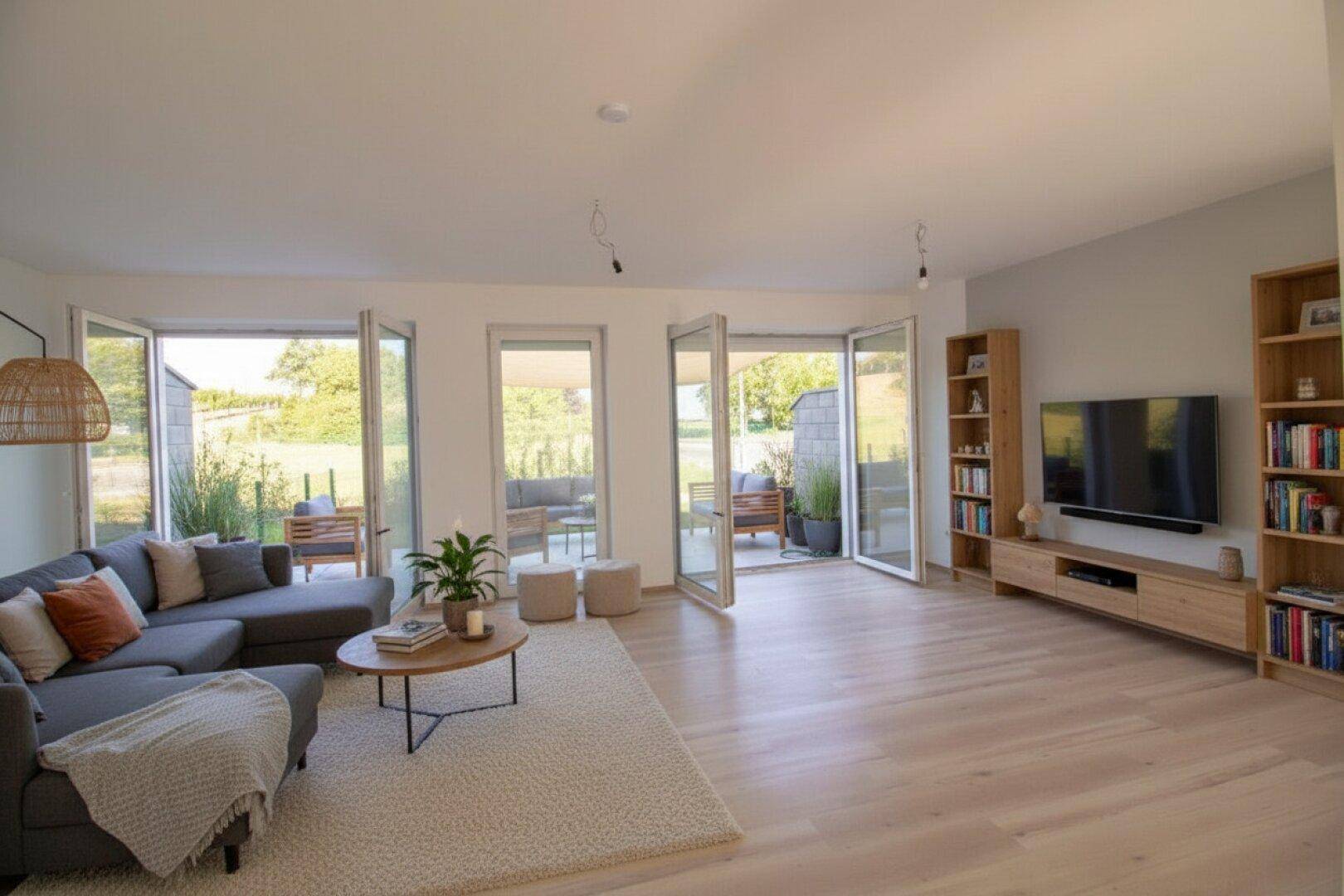 Lichtdurchflutetes Wohnzimmer mit modernem Interieur, Bücherregalen und Zugang zu mehreren Terrassenbereichen.