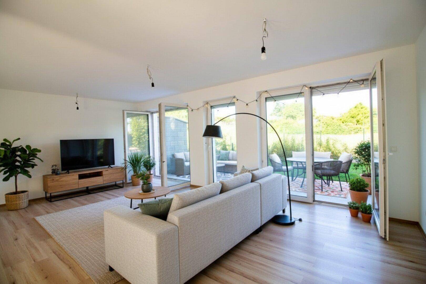 Helles Wohnzimmer mit modernem Sofa, Holzboden und großen Fenstern, die zur Terrasse führen.