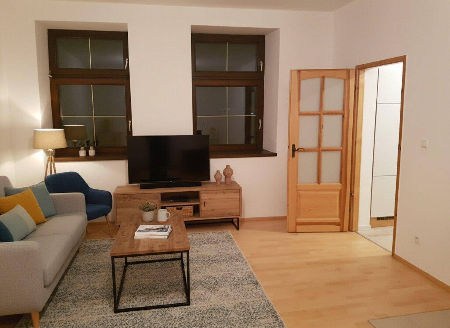 Wohnzimmer mit hellem Holzfußboden, modernem Sofa und traditionellen Holzfenstern.