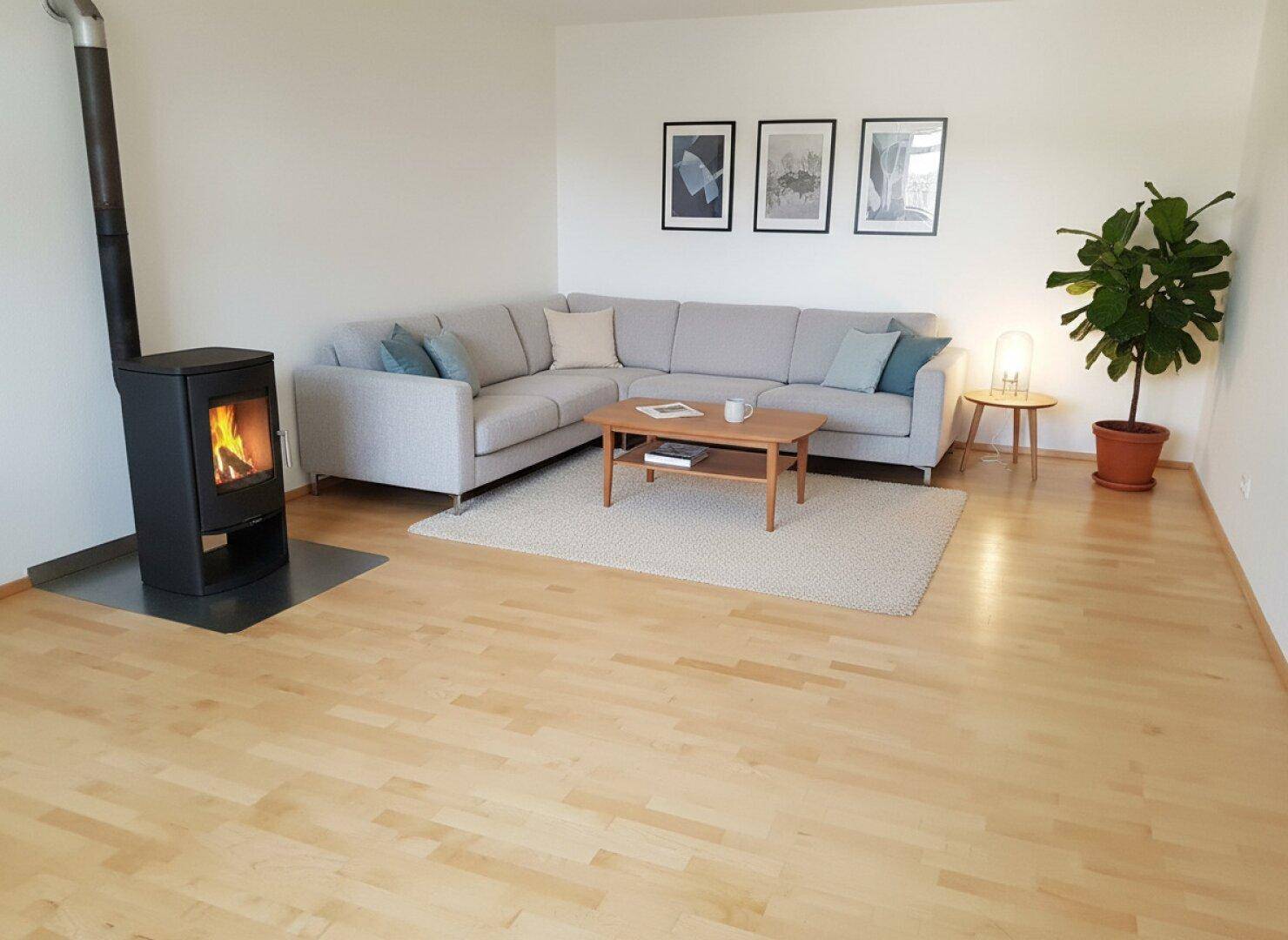 Helles Wohnzimmer mit modernem Ecksofa, Holzboden und gemütlichem Kaminofen.