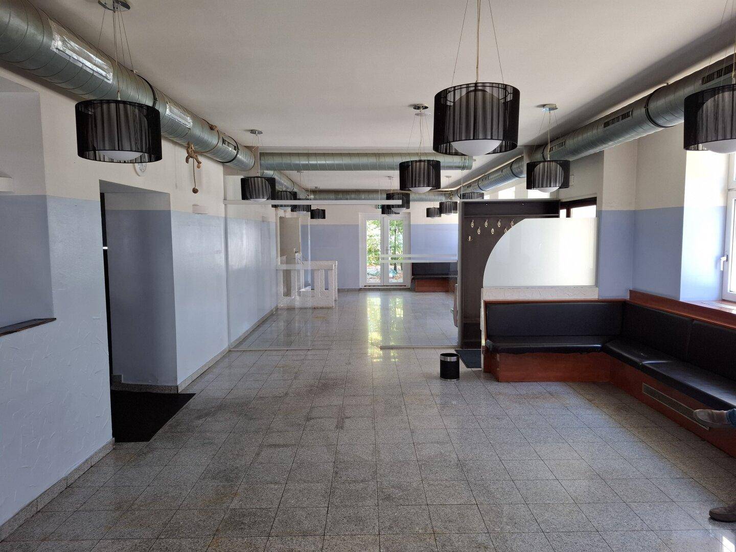 Großer, offener Gewerberaum mit Fliesenboden, sichtbaren Lüftungsrohren und modernen Hängelampen.