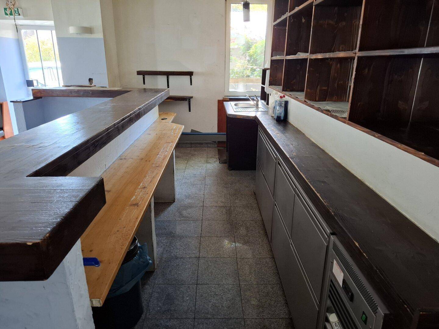 Bar-Bereich mit Holztheke, Regalen und Fliesenboden, bereit für die Einrichtung.