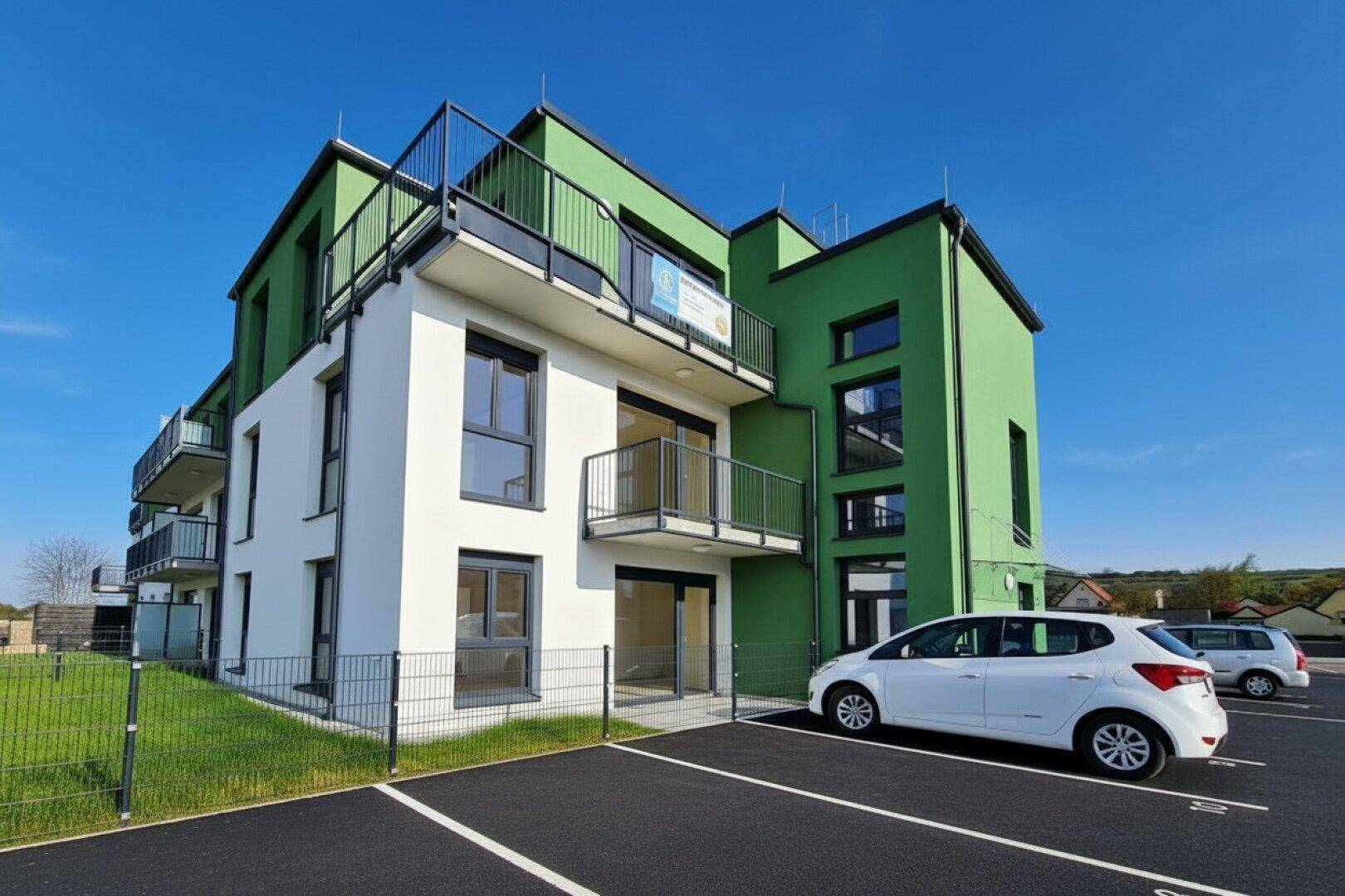 Modernes Neubaugebäude mit grüner und weißer Fassade sowie Balkonen und Außenparkplätzen.