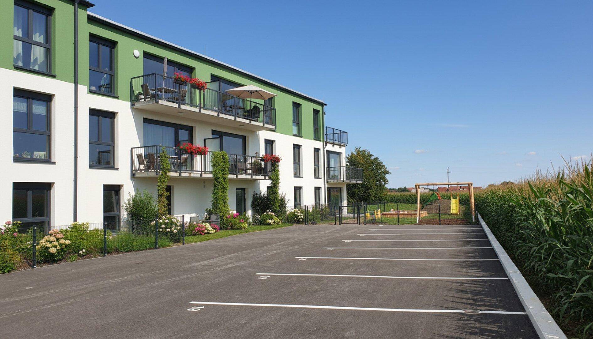 Ansicht des modernen Wohngebäudes mit Balkonen, Parkplätzen und einem angrenzenden Kinderspielplatz.