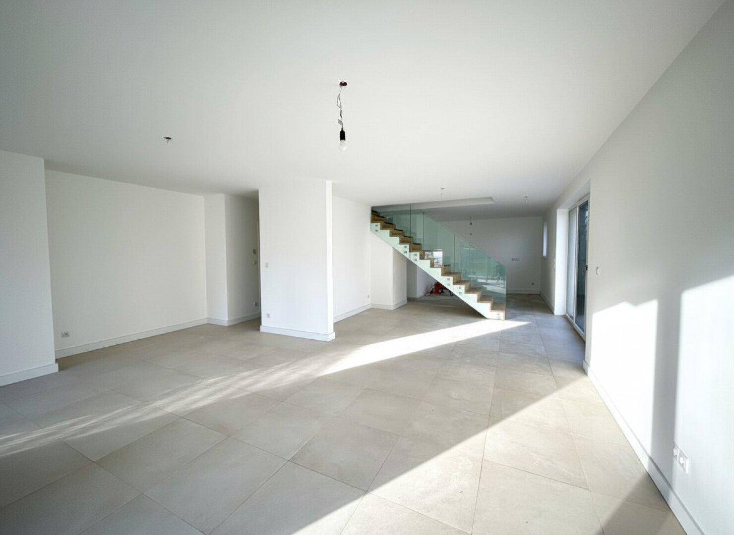Offener Wohnbereich mit hellem Fliesenboden, viel Tageslicht und eleganter Treppe.