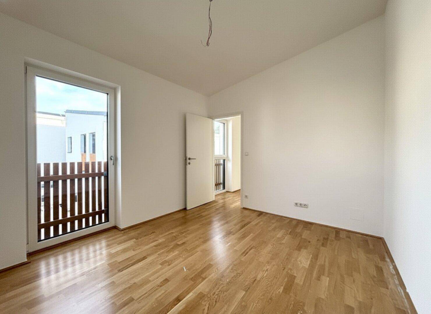 Helles Schlafzimmer mit Holzparkettboden und direktem Zugang zum Balkon.