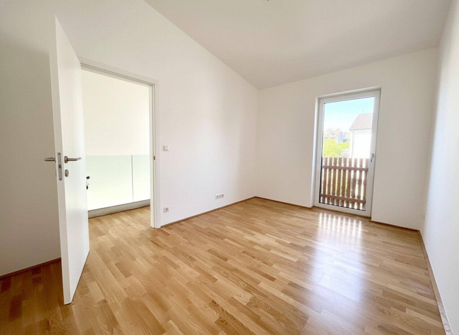 Freundliches Zimmer mit Holzparkett und Balkontür, ideal als Schlaf- oder Arbeitszimmer.