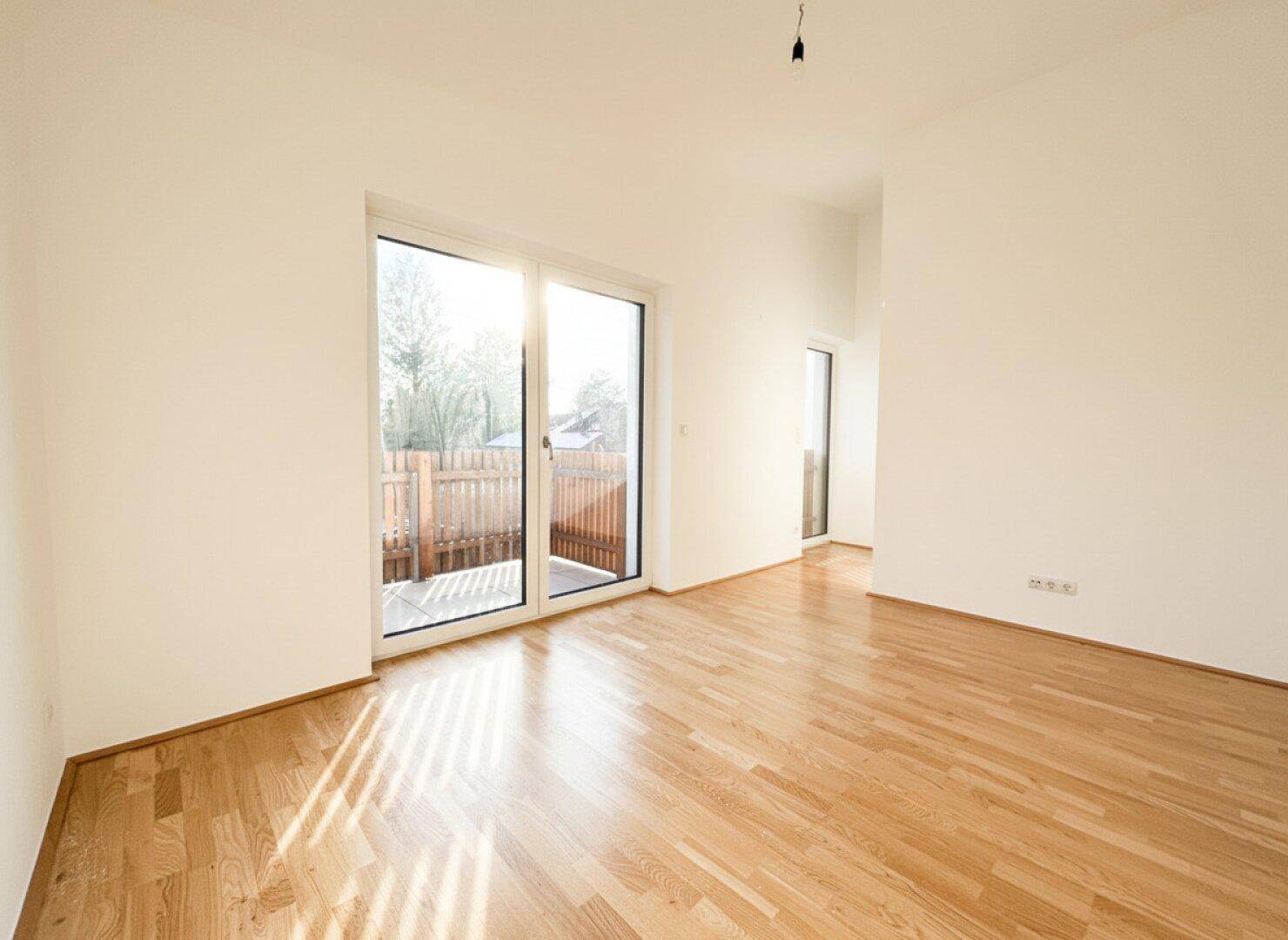 Geräumiger Raum mit Holzparkett und großer Schiebetür zum Außenbereich.