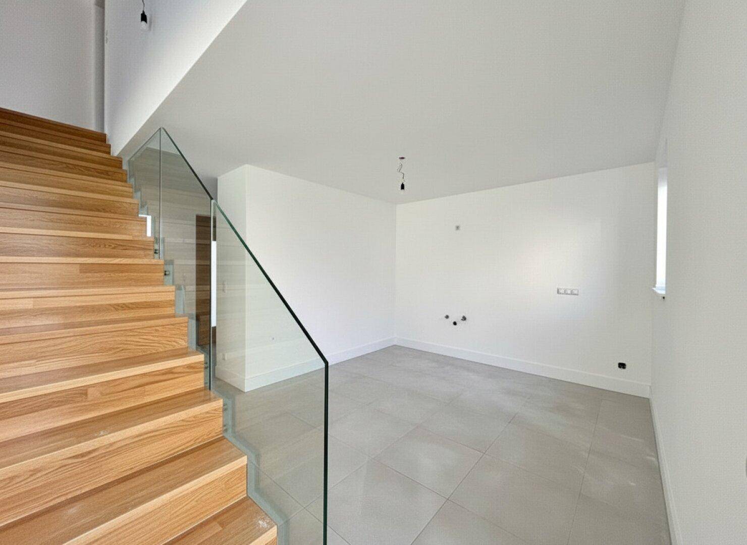 Moderner Eingangsbereich mit Holztreppe, Glasgeländer und hellem Fliesenboden.
