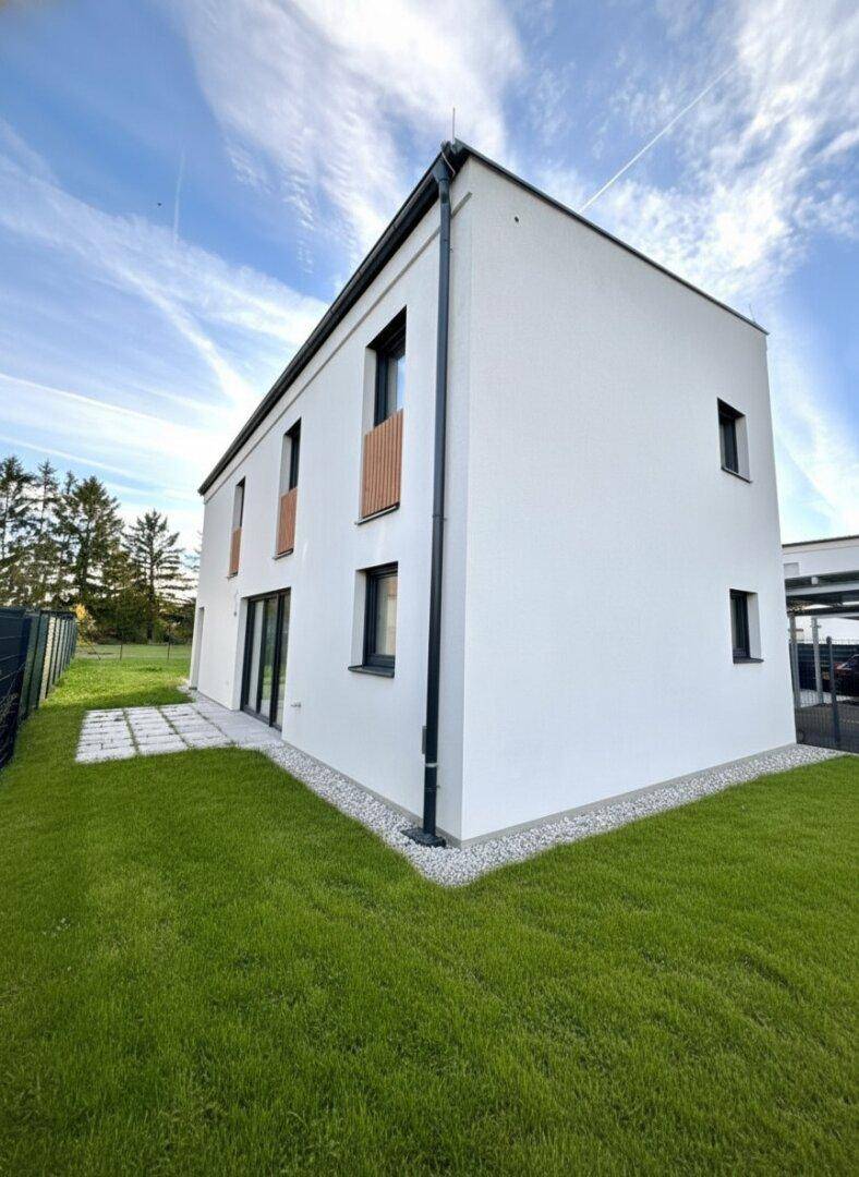 Kleiner, gepflegter Gartenbereich mit Rasenfläche und gepflastertem Weg am Neubau.