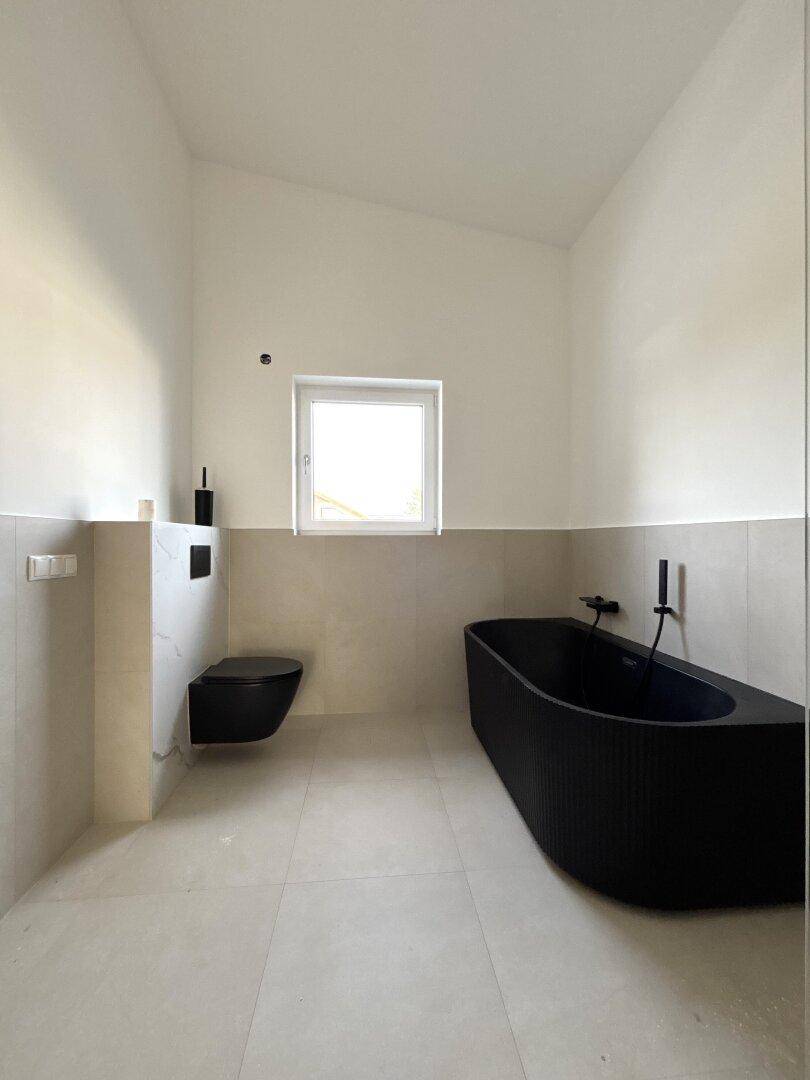Modernes Badezimmer mit freistehender schwarzer Badewanne, Wand-WC und Fenster.