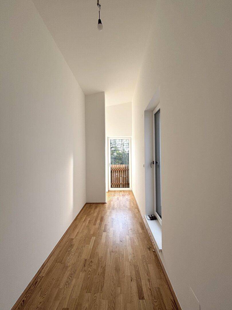 Schmaler Flur mit Holzparkett und Zugang zu einem kleinen Balkon.
