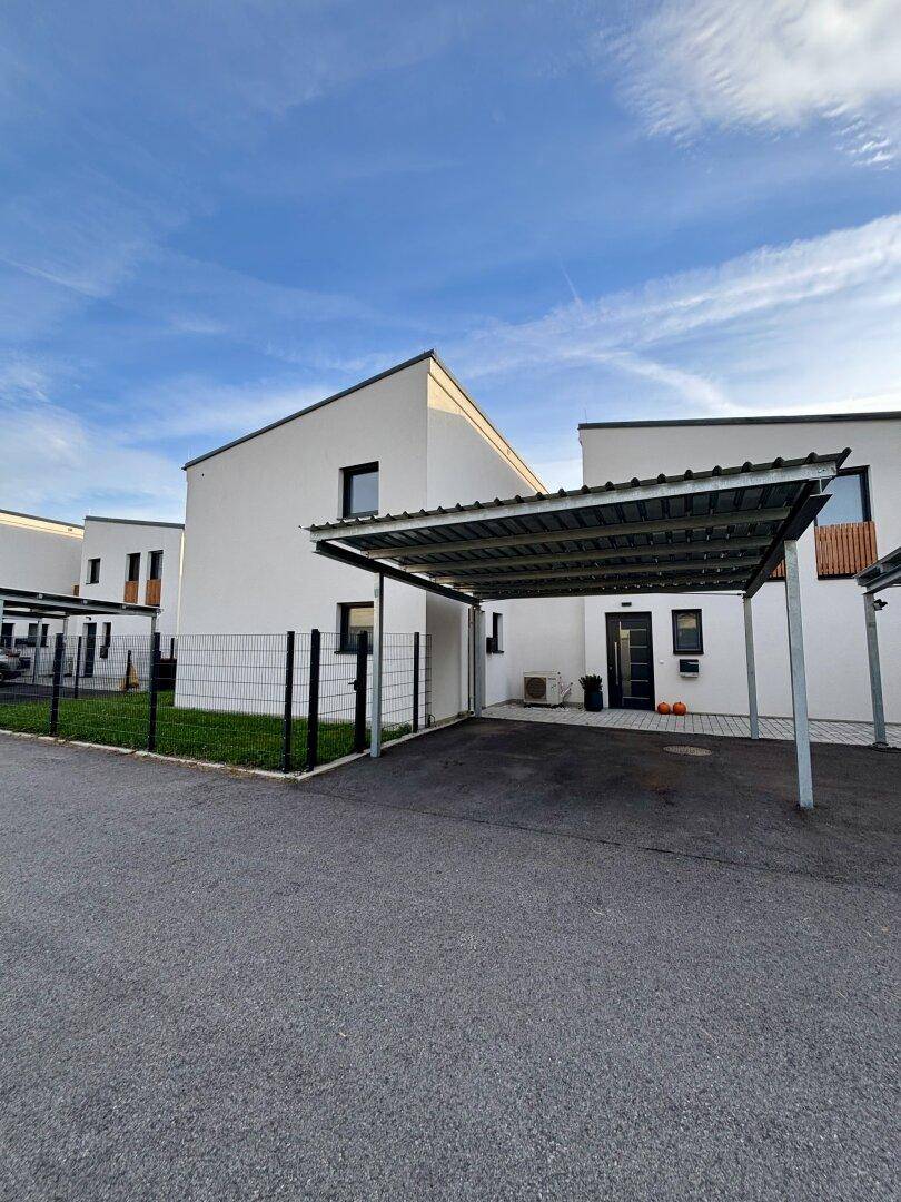 Moderne Reihenhäuser mit Carports und gepflegten Vorgärten unter blauem Himmel.
